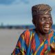 Elderly man joyfully smiling wearing Yoruba attire and cap on Lagos beach.