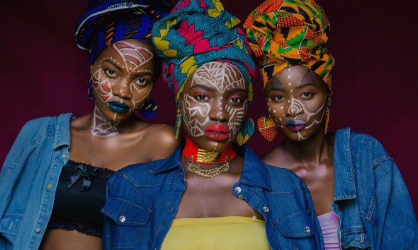 Three women wearing colorful headwraps and face paint, capturing cultural vibrancy in Lagos, Nigeria.