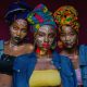 Three women wearing colorful headwraps and face paint, capturing cultural vibrancy in Lagos, Nigeria.