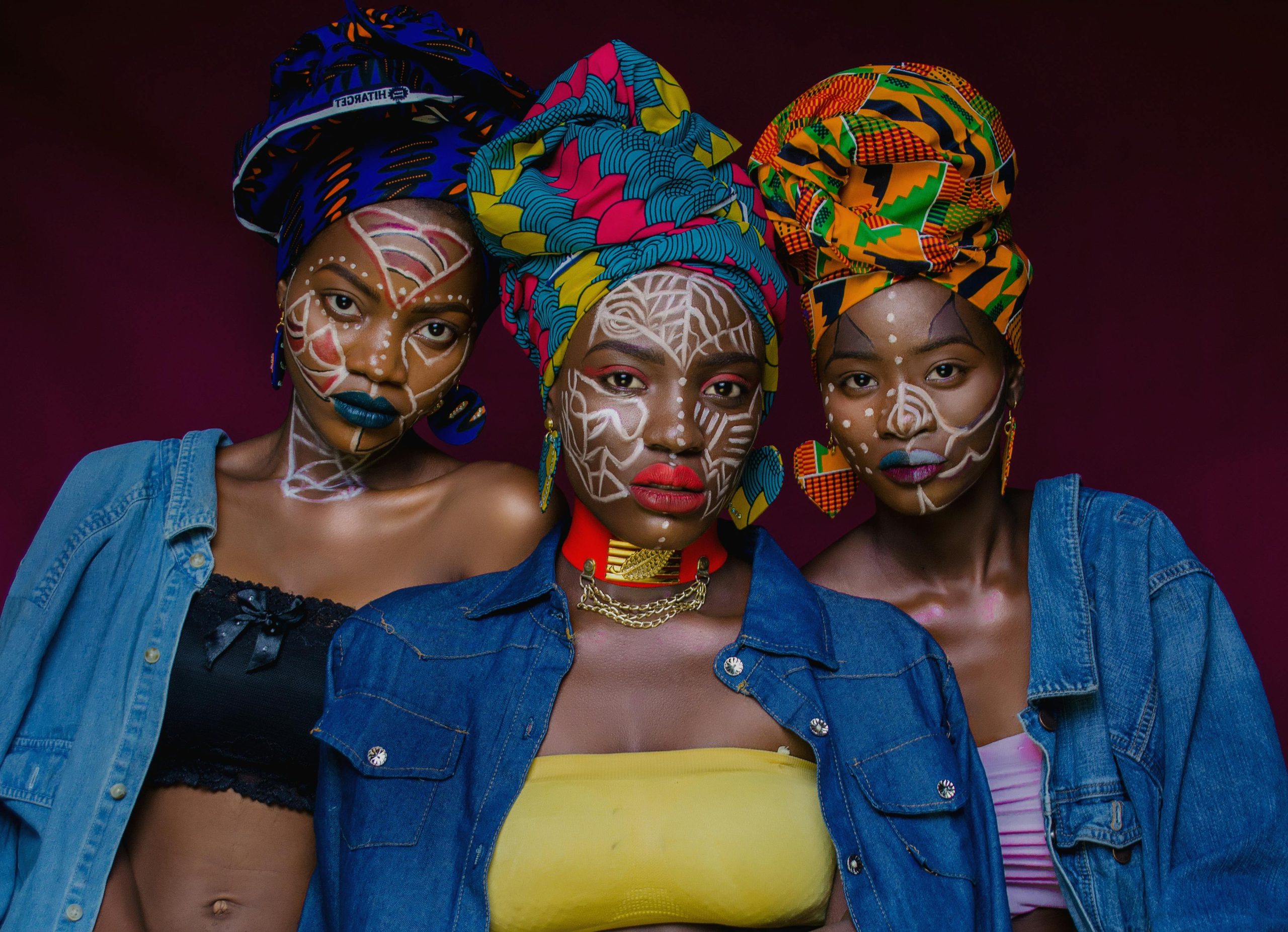 Three women wearing colorful headwraps and face paint, capturing cultural vibrancy in Lagos, Nigeria.