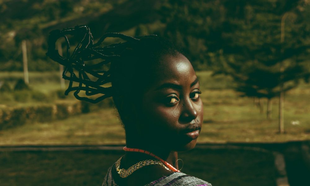 A woman with braided hair in a natural outdoor setting gazing back.