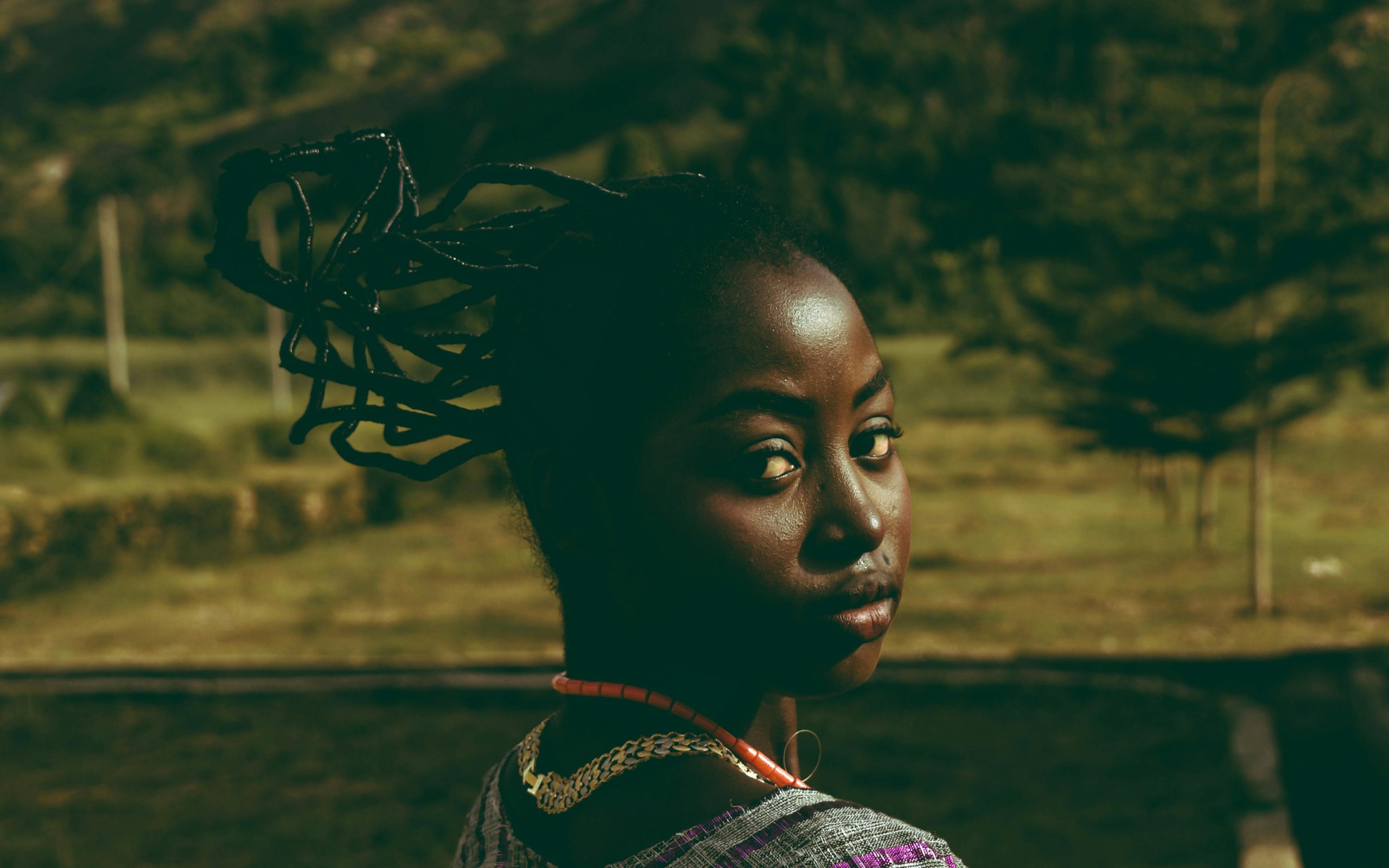 A woman with braided hair in a natural outdoor setting gazing back.