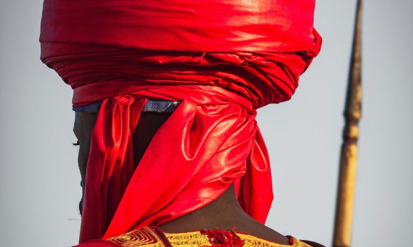 Man in traditional African attire with a striking red turban, symbolizing cultural heritage.