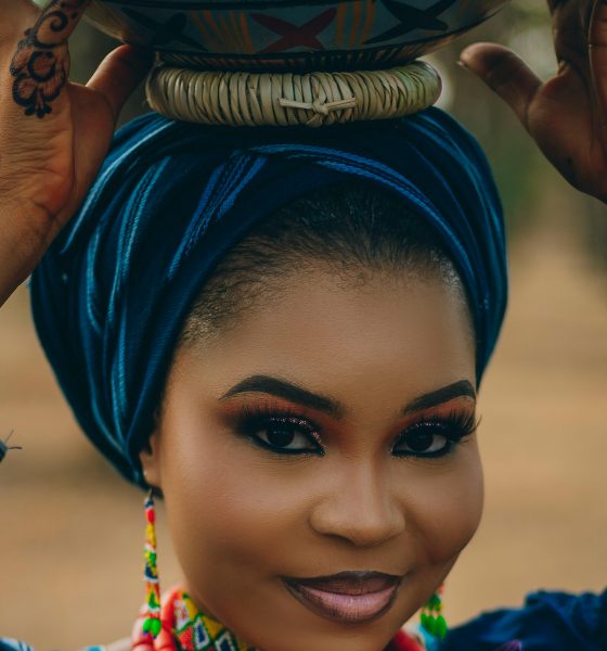 Portrait of a woman in vibrant traditional Nigerian attire balancing a pot on her head.