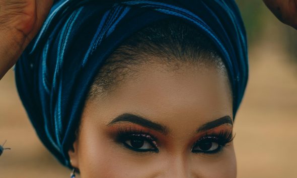 Portrait of a woman in vibrant traditional Nigerian attire balancing a pot on her head.