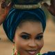 Portrait of a woman in vibrant traditional Nigerian attire balancing a pot on her head.