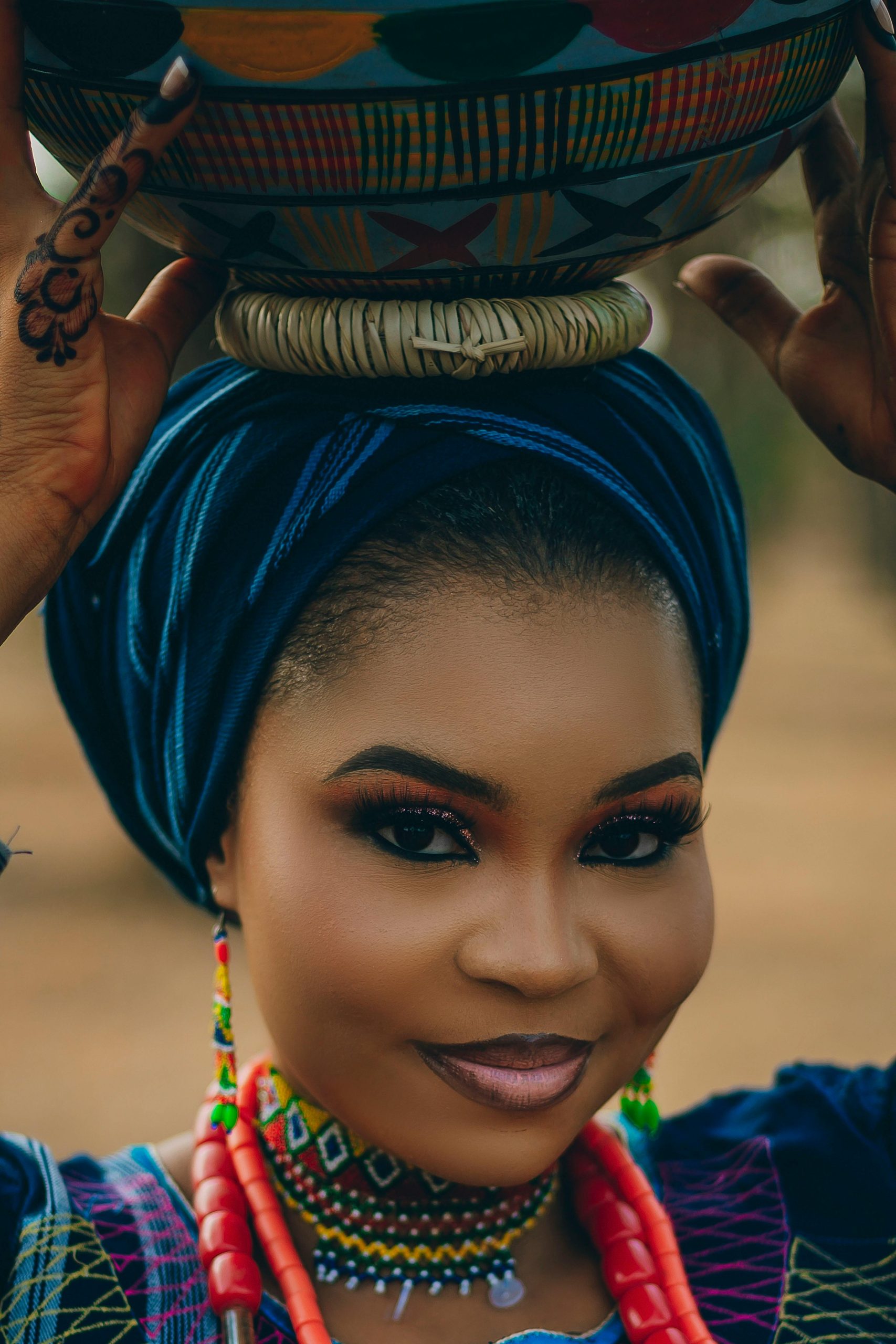 Portrait of a woman in vibrant traditional Nigerian attire balancing a pot on her head.