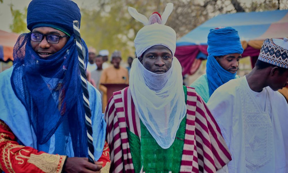 Men wearing colorful traditional African clothing at an outdoor gathering.