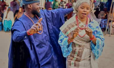 Vibrant celebration with African couple in colorful traditional outfits dancing joyfully outdoors.