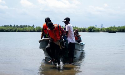 Group of people disembarking a boat onto a seashore with lush greenery in the background.