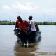 Group of people disembarking a boat onto a seashore with lush greenery in the background.