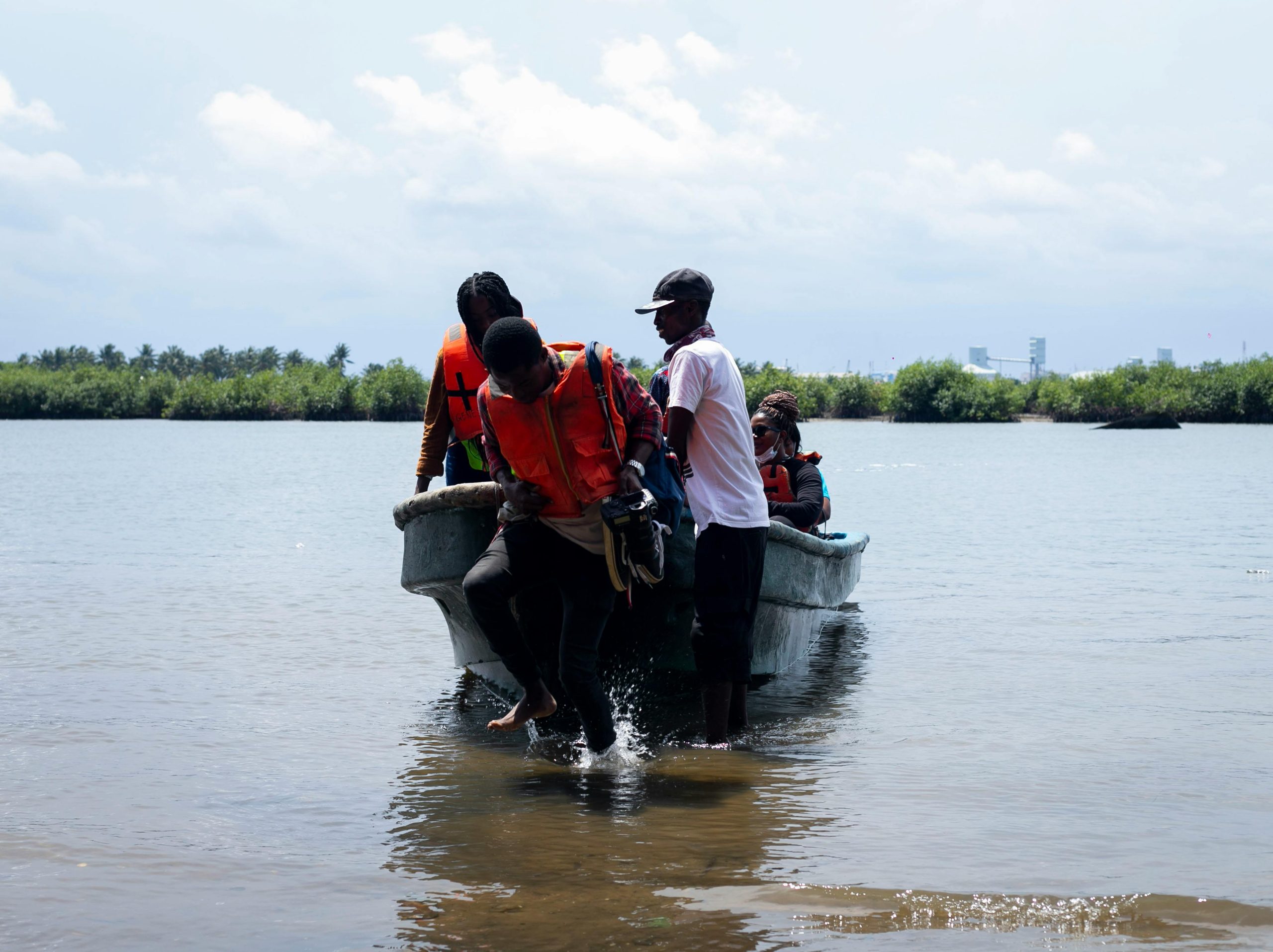 Group of people disembarking a boat onto a seashore with lush greenery in the background.