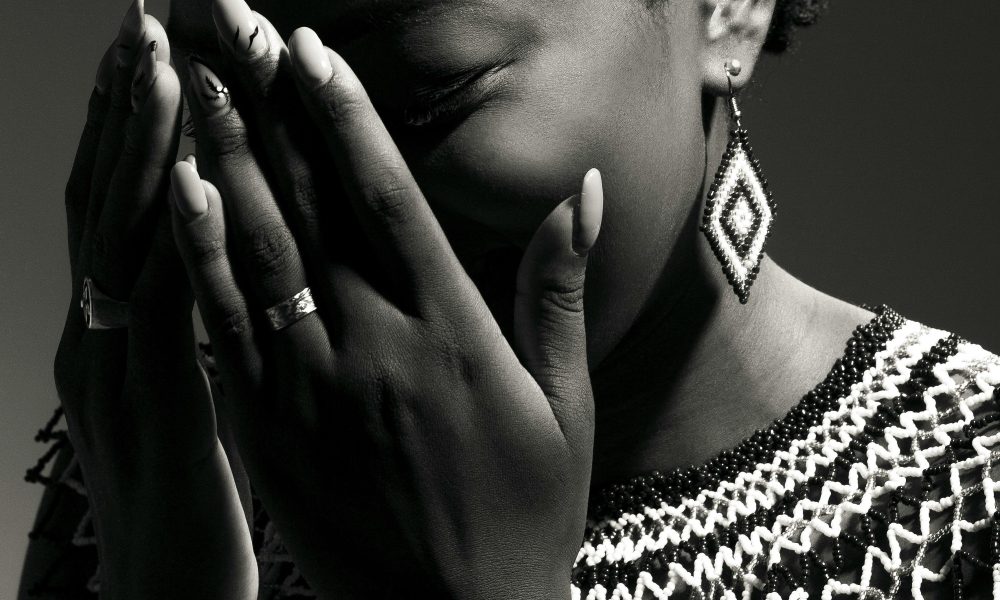 A stunning black and white portrait of a woman wearing traditional jewelry, covering her face with her hands.