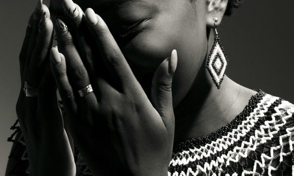A stunning black and white portrait of a woman wearing traditional jewelry, covering her face with her hands.