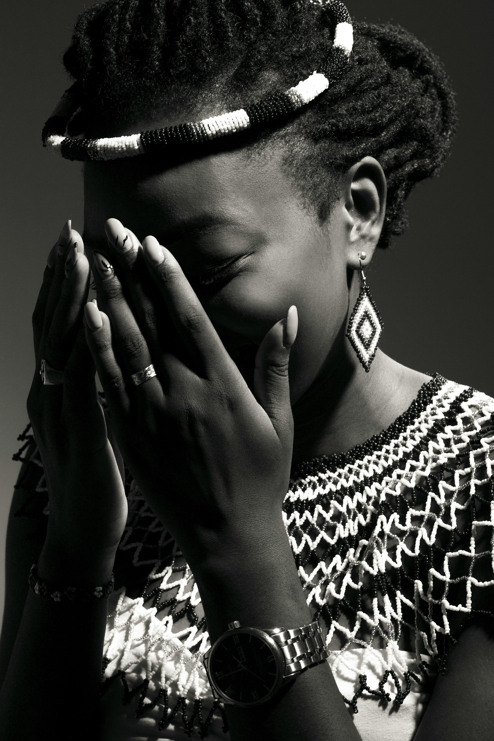A stunning black and white portrait of a woman wearing traditional jewelry, covering her face with her hands.